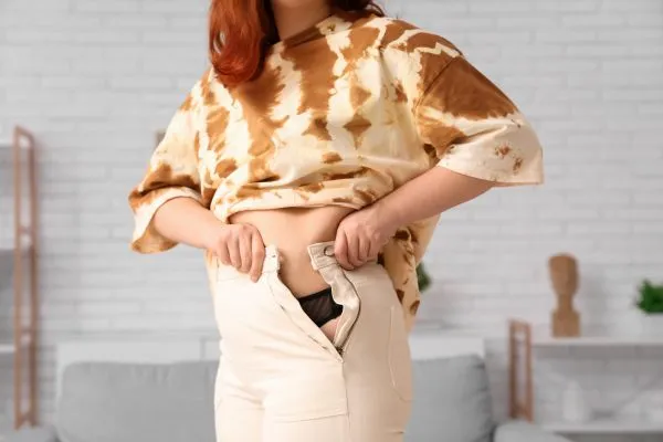 Image of woman trying to do her trousers up after pregnancy weight gain Dunstable
