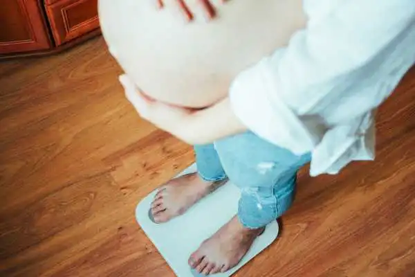 Image of woman weighing herself and experiencing weight gain through pregnancy Dunstable